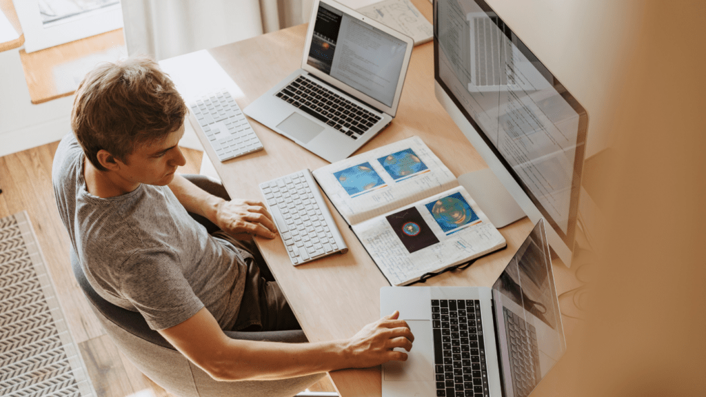 a person sitting at a desk with two computers and a laptop