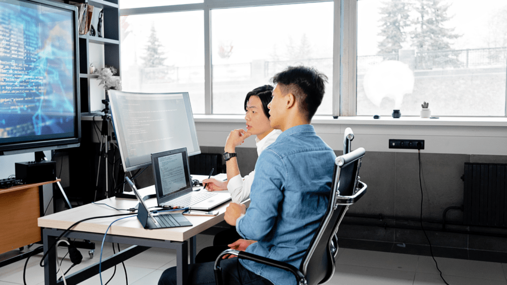 two people sitting at a desk in front of a computer screen