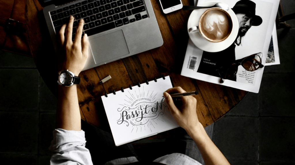 a person working on a laptop at a table with a notebook and a cup of coffee